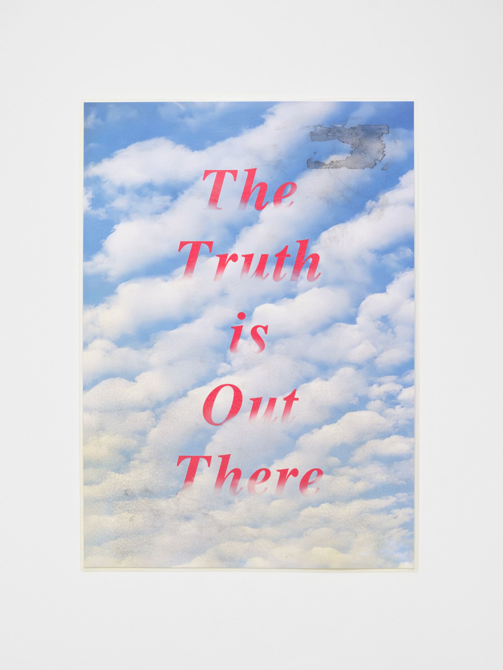 Close-up of a rectangular poster depicting a blue sky with white clouds. The text