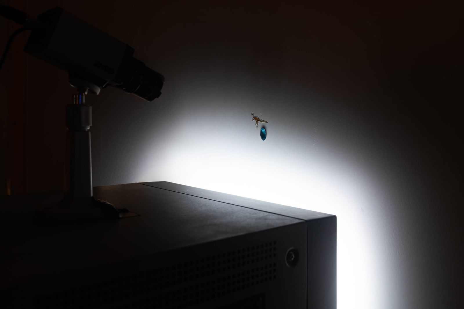 a CCTV camera positioned on top of the CRT is aimed at two small stickers (one of a dinosaur and the other a blue 3d gem) on the rear of the wall